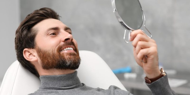 Man,Looking,At,His,New,Dental,Implants,In,Mirror,Indoors